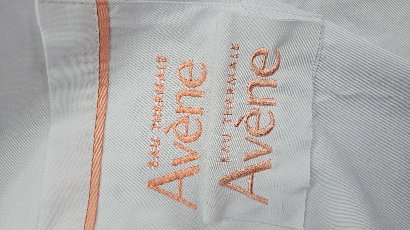 Broderie halat logo brand premium Avene — personalizare textilă farmaceutică